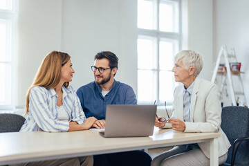 Obraz premium Mature female working as an insurance agent, advising a young couple about the home insurance.