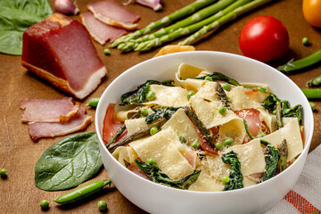 Pasta pappardelle with Italian prosciutto or jamon and spinach, parmesane, asparagus . Wooden background. Close up.