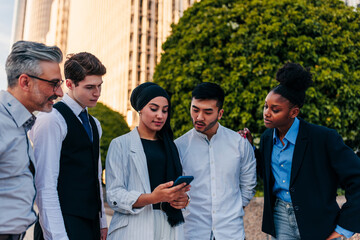 Business team outdoors looking at coworkers smartphone