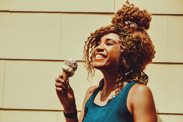 young adult woman afro hair eating ice cream outdoors summertime looking away at copy space shot
