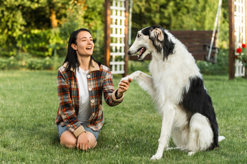 The woman in the backyard is teaching her dog to give a paw