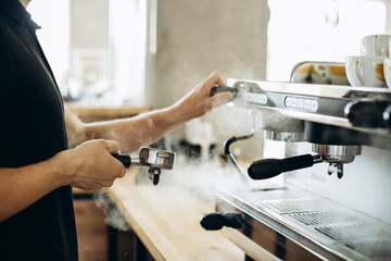 Barista preparing coffee at the coffee machine and holding portafilter