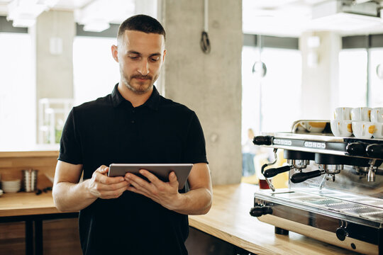 Man barista with tablet standing by the counter - Powered by Adobe