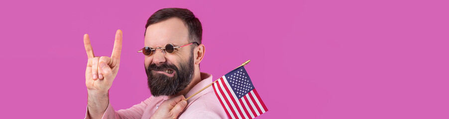 Portrait of a satisfied young man with a beard with an American flag on a red studio background....