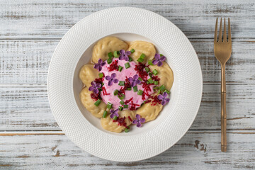 Appetizing dumplings stuffed with potatoes and mushrooms with sour cream decorated with beets and lilac flowers