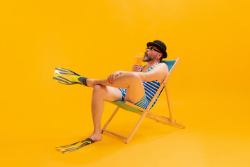 Studio shoot of cool funny beachgoer, man in vintage striped swimsuit and bowler hat sitting in...