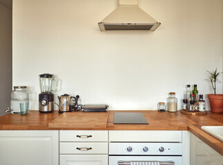 Horizontal shot of modern Mediterranean interior style design light white kitchen equipped domestic area for cooking with induction stove, cozy flat indoors, furniture with utensils, wooden tabletop