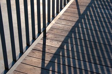 Striped shadow of a metal fence on wooden floor