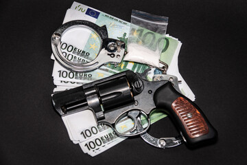 Revolver, euro, handcuffs and a bag of white powder on a black background. The concept of punishment for the manufacture and sale of drugs.