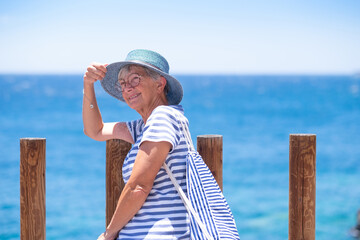 Portrait of attractive smiling caucasian senior woman sitting outdoors at sea enjoying summer holidays. Horizon over water