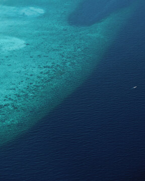 Vista aérea de un arrecife de coral del océano y de los tonos de azul con un barco pequeño navegando