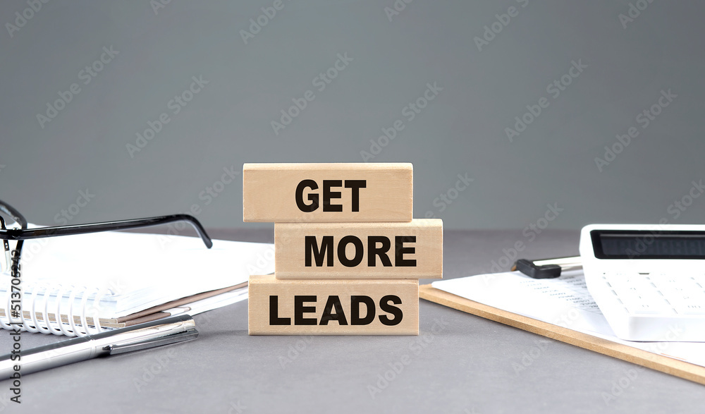 Poster get more leads text on wooden block with notebook,chart and calculator, grey background