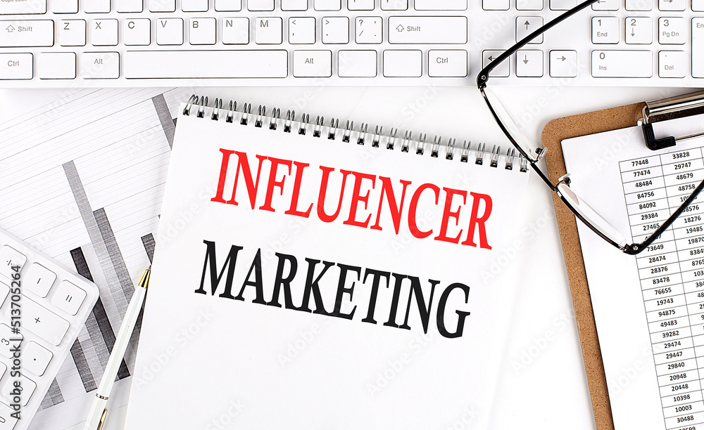 Poster text influencer marketing on office desk table with keyboard, notepad and analysis chart on white ba