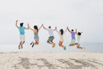 Full length rear photo of excited carefree fellows hold hands jumping sea seaside outdoors