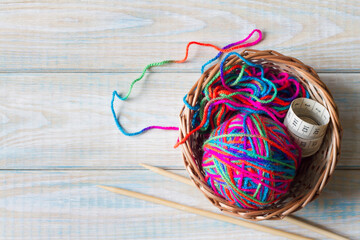 Yarn of rainbow colors and knitting needles on light wooden background