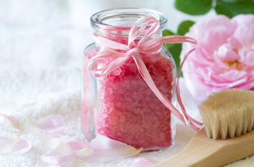 Rose bath salt  in glass bottle, body care accessories and fresh rose petals on light background, spa concept 