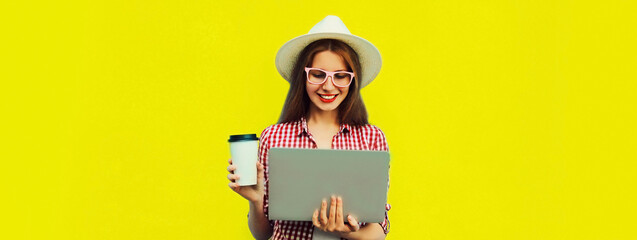 Portrait of modern young woman working with laptop drinking coffee on yellow background