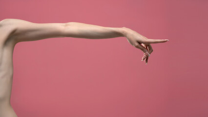 Young woman's stretched skinny arm and touching imaginary product with index finger. Isolated on pink background