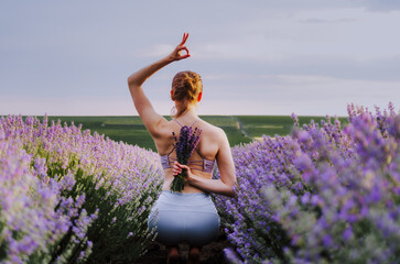 Woman in active wear holding a lavender bouquet in a yoga pose, in a lavender field at sunset with ok sign overhead
