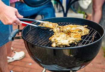 young man chef cooking chicken meat on grill outdoor