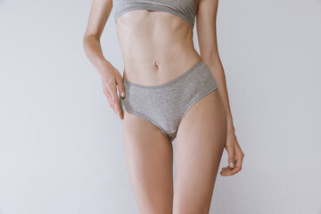 Cropped image of slender female body, belly and buttocks in underwear isolated over grey studio...