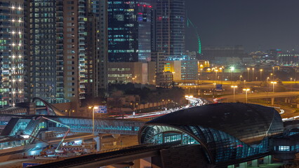 Fototapeta na wymiar Futuristic building of Dubai metro station and luxury skyscrapers behind in Dubai Marina aerial night timelapse