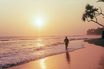 Male model, traveler walking the beach with sunset and ocean background, holiday tropical landscape.