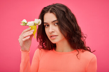 Portrait of young woman with curly hair looking at camera on pink background and holding menstrual...
