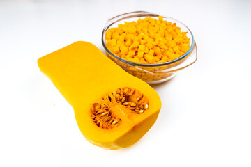 Half a of an Butternut Squash (Cucurbita moschata) pumpkin and a bowl of small diced pumpkin on white  background. Autumn vegetables for proper nutrition. Copy space. Flat lay.