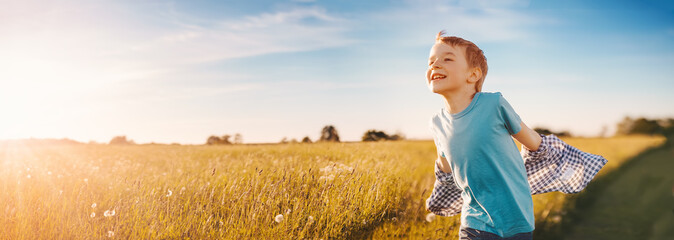 Happy child running through a summer field at evening sunset - 513714259