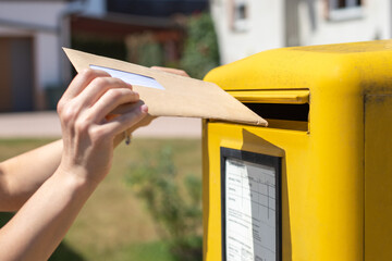 person throws letter in yellow mailbox
