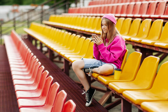 A teenage girl sits on the school bleachers and writes a message on her phone in her free time