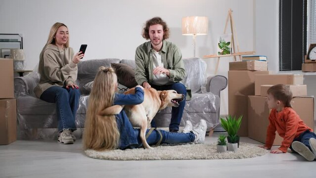 family of homeowners rejoice in the move and shoot a video or photo on mobile phone, parents with children and a dog are relaxing in a new house