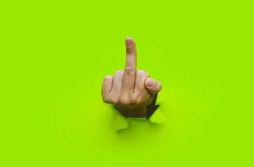 Middle finger of left hand, insulting gesture. Torn hole in green paper. Fuck you concept....