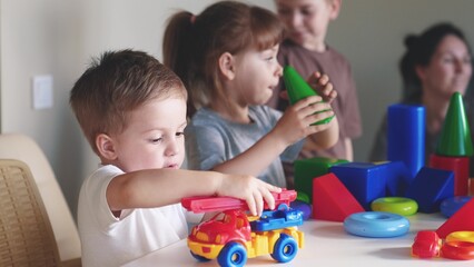 Obraz premium little boy and baby girl play in kindergarten. a group of children play toys cubes and cars on the table in kindergarten. happy family preschool education concept. indoor nursery baby toddler home
