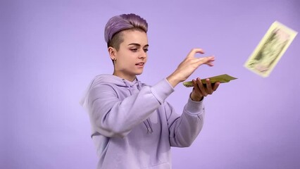 Happy young adult person gen Z with trendy appearance throwing bunch money around, scattering banknotes, raising hands up, rejoicing luck lottery, boasting money profit isolated on purple background