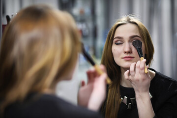 A young girl does make-up in a beauty salon. The girl in front of the mirror is making up. Beauty saloon.
