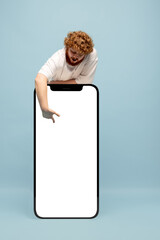 Red-headed man standing next to huge 3d model of smartphone with empty white screen isolated on...