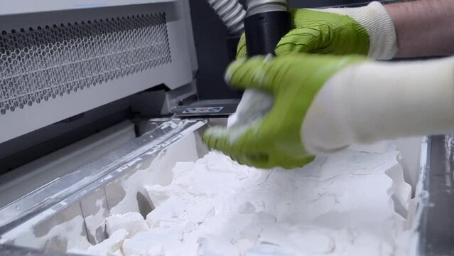 A man working with a working vacuum cleaner to clean the white powder of polyamide from a model printed on a 3D printer inside a 3D printer. Cleaning objects printed on an industrial powder 3D printer