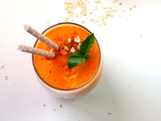 A glass of papaya and oatmeal smoothie, straws for cocktails, green leaves, oat flakes. Top view on a white background. (Selective Focus, Focus on the basil leaves)