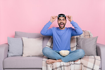 Photo of pretty impressed arabian man wear long sleeve shirt sitting sofa watching movie isolated pink color background