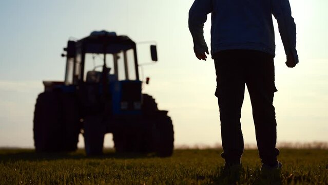Farmer at Dusk. Silhouette young farmer in tractor preparing land with seedbed cultivator at sunset time. Male farmer walking in sunny field. Silhouette agricultural harvest farming by tractor.