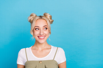 Photo of optimistic blond buns hairdo lady look empty space wear t-shirt overall isolated on blue...