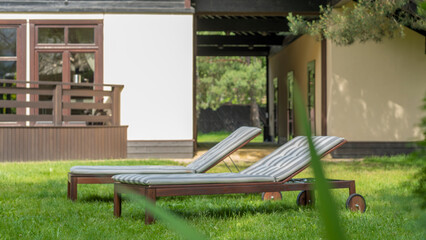 Lounge chairs on the backyard in a beautiful garden. Two empty sunbeds on the grass.