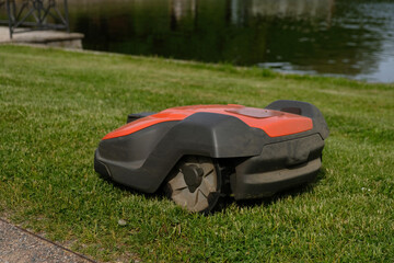 Robotic Lawn Mower on green grass background.Automatic robot lawnmower in modern garden.Green grass trimming with lawn mower. Close-up view of the lawn mower dirty blade after mowing the lawn. 