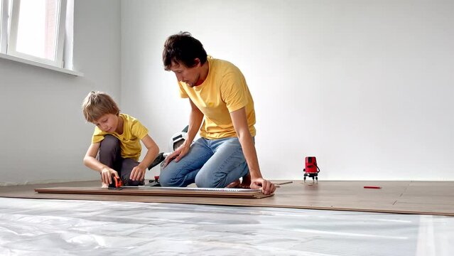 Father and his little son install laminate on the floor in their apartment. DIY concept. Slowmotion video