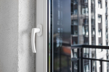 Window frame of a white metal-plastic with a handle and glass through which windows of a residential building are visible