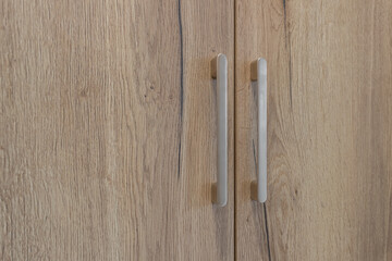 Two handles on the door of a light-colored wooden cabinet
