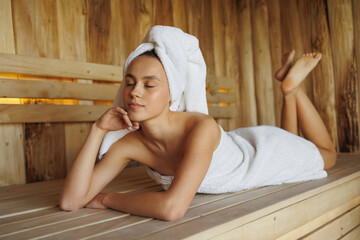 Beautiful young woman with closed eyes lying in wooden sauna