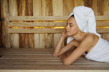 Young woman in white towel lying in wooden sauna